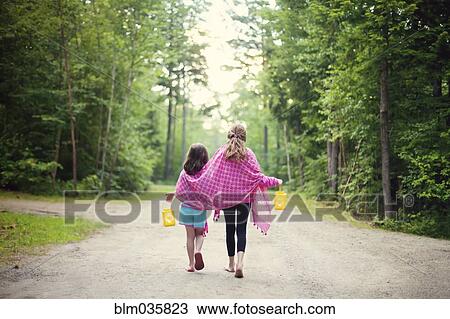 Stock Image - Caucasian sisters walking on dirt road. Fotosearch