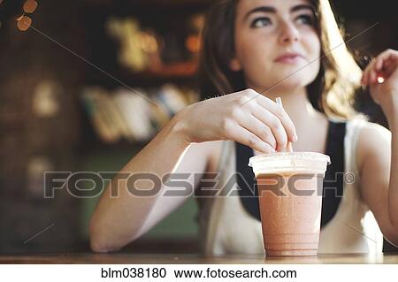 Stock Image - Caucasian teenage girl drinking smoothie in cafe. Fotosearch
