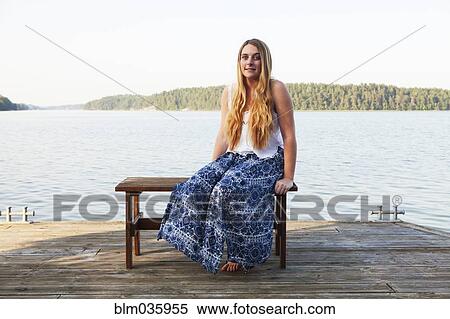 Stock Photography - Caucasian teenage girl sitting on wooden dock at lake. Fotosearch