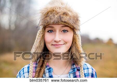 Stock Image - Caucasian teenage girl wearing fur hat in field. Fotosearch