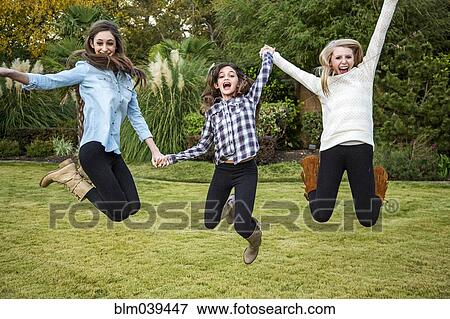 Stock Photo - Caucasian teenage girls jumping for joy in backyard. Fotosearch