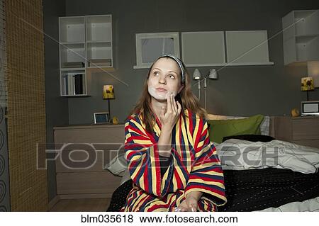 Stock Photo - Caucasian woman applying moisturizer to face in bedroom. Fotosearch