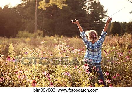 Stock Image - Caucasian woman cheering with arms outstretched in field. Fotosearch