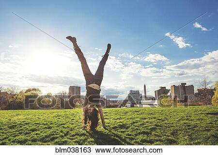 Stock Image - Caucasian woman doing handstand in urban park. Fotosearch