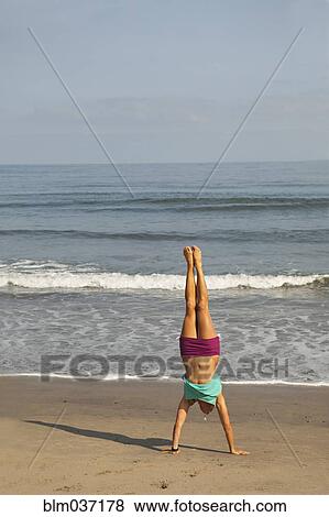 Stock Photo - Caucasian woman doing handstand on beach. Fotosearch