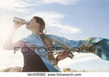 Stock Image - Caucasian woman drinking from bottle in wind. Fotosearch