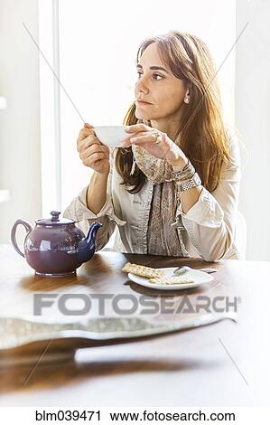 Stock Image - Caucasian woman drinking tea at table. Fotosearch