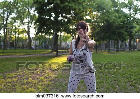 Stock Photograph - Caucasian woman gesturing peace sign in park. Fotosearch