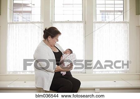 Picture - Caucasian woman holding baby granddaughter in windowsill. Fotosearch