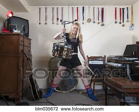 Stock Image - Caucasian woman holding drum upside-down in living room. Fotosearch