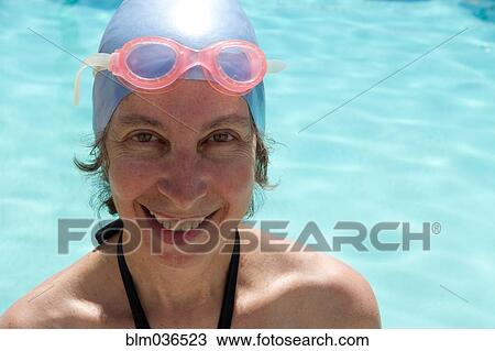 Stock Image - Caucasian woman in goggles and swim cap by swimming pool. Fotosearch