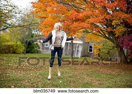 Stock Photo - Caucasian woman jumping for joy in backyard. Fotosearch