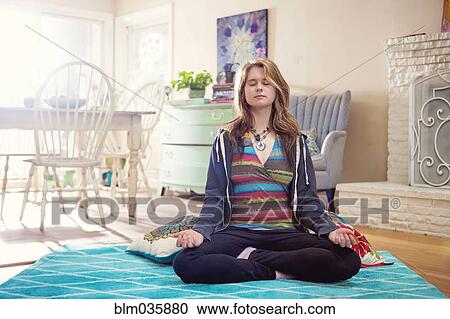 Stock Image - Caucasian woman meditating in living room. Fotosearch