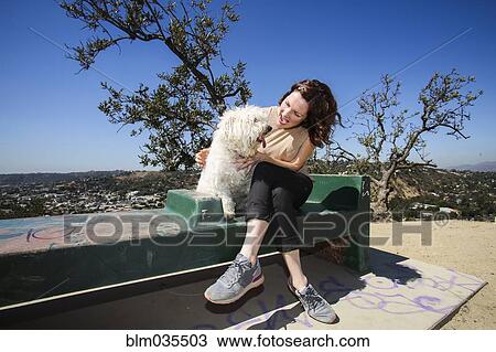Stock Image - Caucasian woman petting dog on hilltop bench. Fotosearch