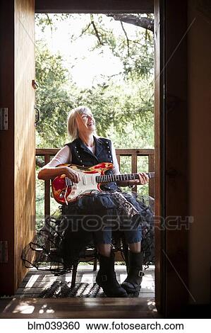Stock Image - Caucasian woman playing electric guitar on porch. Fotosearch