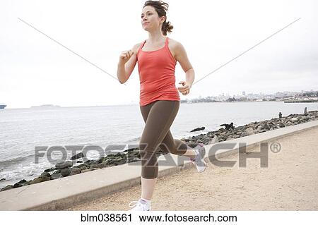 Stock Image - Caucasian woman running on waterfront. Fotosearch