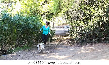 Picture - Caucasian woman running with dog on dirt path. Fotosearch