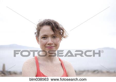 Stock Image - Caucasian woman smiling on rocky beach. Fotosearch