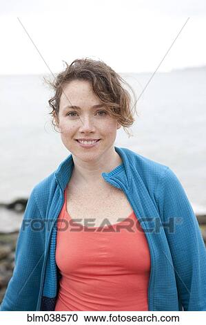 Stock Image - Caucasian woman smiling on rocky beach. Fotosearch