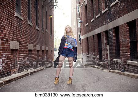 Stock Image - Caucasian woman standing in city alleyway. Fotosearch