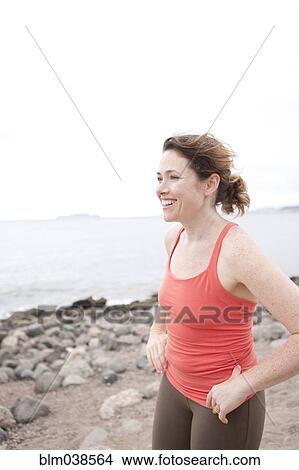 Picture - Caucasian woman standing on rocky beach. Fotosearch