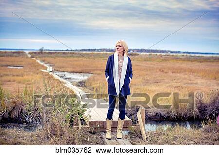 Stock Image - Caucasian woman standing on walkway in rural field. Fotosearch