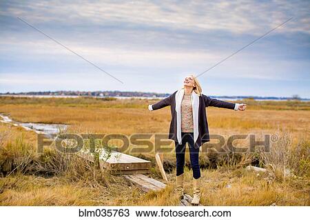 Stock Image - Caucasian woman standing on walkway in rural field. Fotosearch