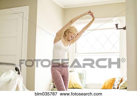 Stock Photo - Caucasian woman stretching in bedroom. Fotosearch