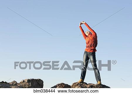 Picture - Caucasian woman stretching on rocky hilltop. Fotosearch
