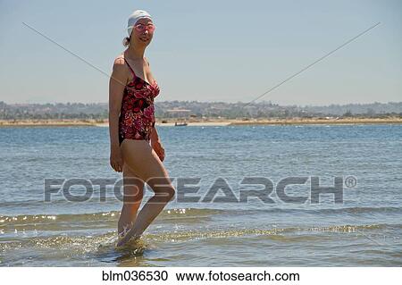 Stock Image - Caucasian woman walking in waves on beach. Fotosearch
