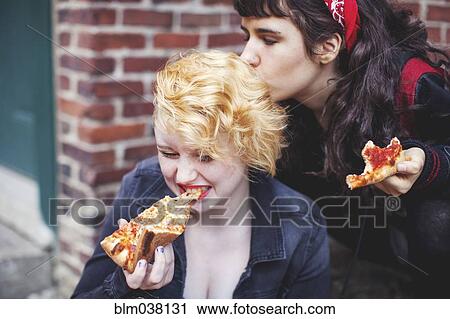 Stock Image - Caucasian women eating pizza outdoors. Fotosearch