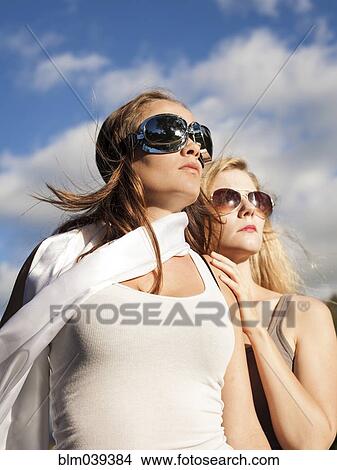 Picture - Caucasian women wearing sunglasses and looking up. Fotosearch