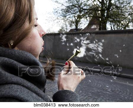 Stock Image - Close up of Caucasian woman blowing dandelion seeds. Fotosearch