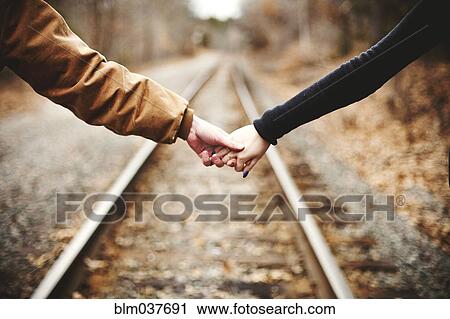 Stock Image - Close up of couple holding hands on railroad tracks. Fotosearch