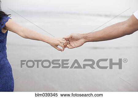 Stock Photography - Close up of couple holding hands on beach. Fotosearch