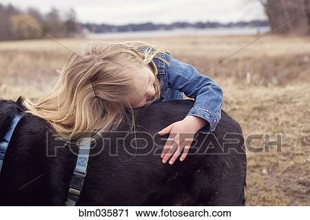 Stock Image - Close up of girl hugging dog in rural field. Fotosearch