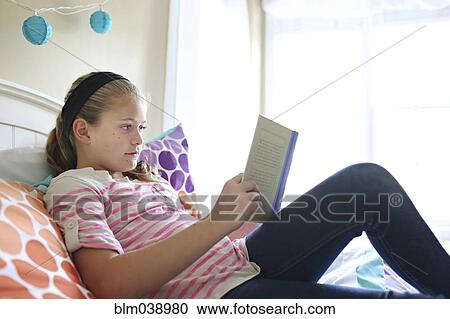 Stock Image - Close up of girl reading book on bed. Fotosearch