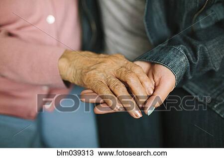Stock Image - Close up of grandmother and granddaughter holding hands. Fotosearch