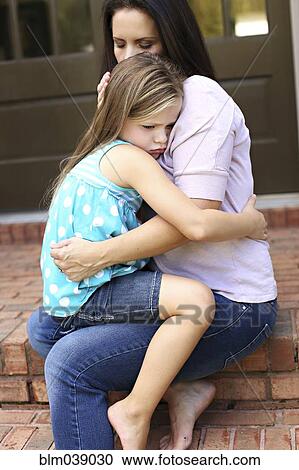 Stock Image - Close up of mother comforting daughter on front stoop. Fotosearch