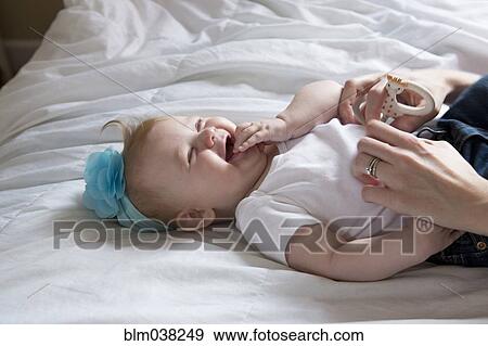 Stock Photo - Close up of mother tickling baby girl on bed. Fotosearch