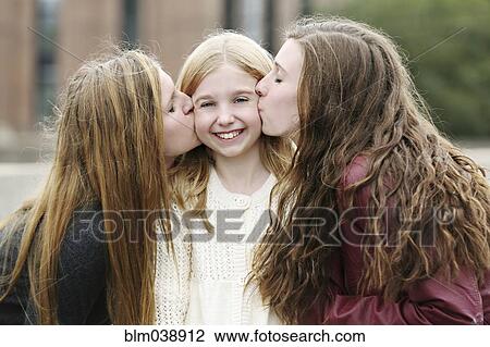 Stock Image - Close up of smiling sisters kissing outdoors. Fotosearch