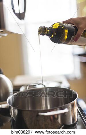Stock Photo - Close up of woman pouring olive oil into pot. Fotosearch