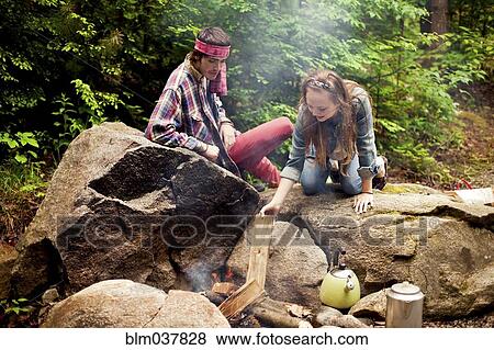 Stock Photo - Couple building campfire in forest. Fotosearch