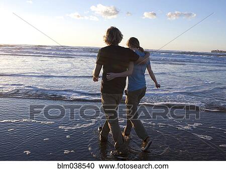 Stock Image - Couple hugging and walking in waves on beach. Fotosearch