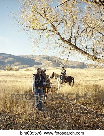 Stock Photograph - Couple leading horses on dirt path. Fotosearch