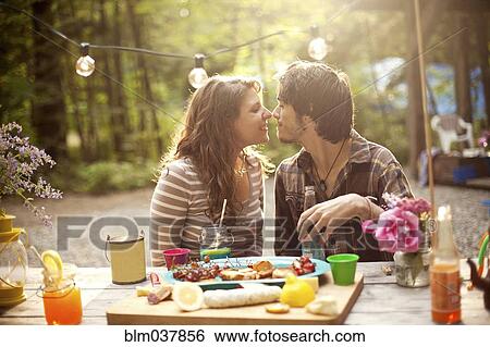 Stock Photograph - Couple rubbing noses at picnic table in forest. Fotosearch