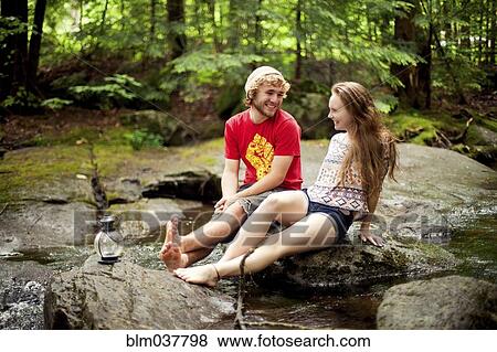 Stock Photo - Couple sitting barefoot on boulders in forest. Fotosearch
