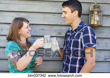 Stock Image - Couple toasting with drinks near wall. Fotosearch