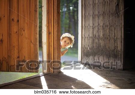Stock Photograph - Curious girl peering around open door. Fotosearch
