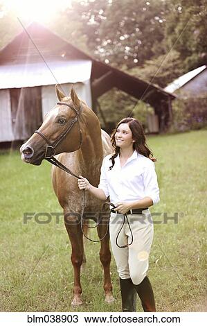 Stock Image - Equestrian woman walking horse in yard. Fotosearch
